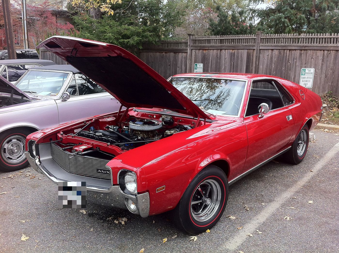 Red 1968 AMC AMX two-seater at a car show with the hood raised on its 390 V8, red-line tires and the AMX grille badge