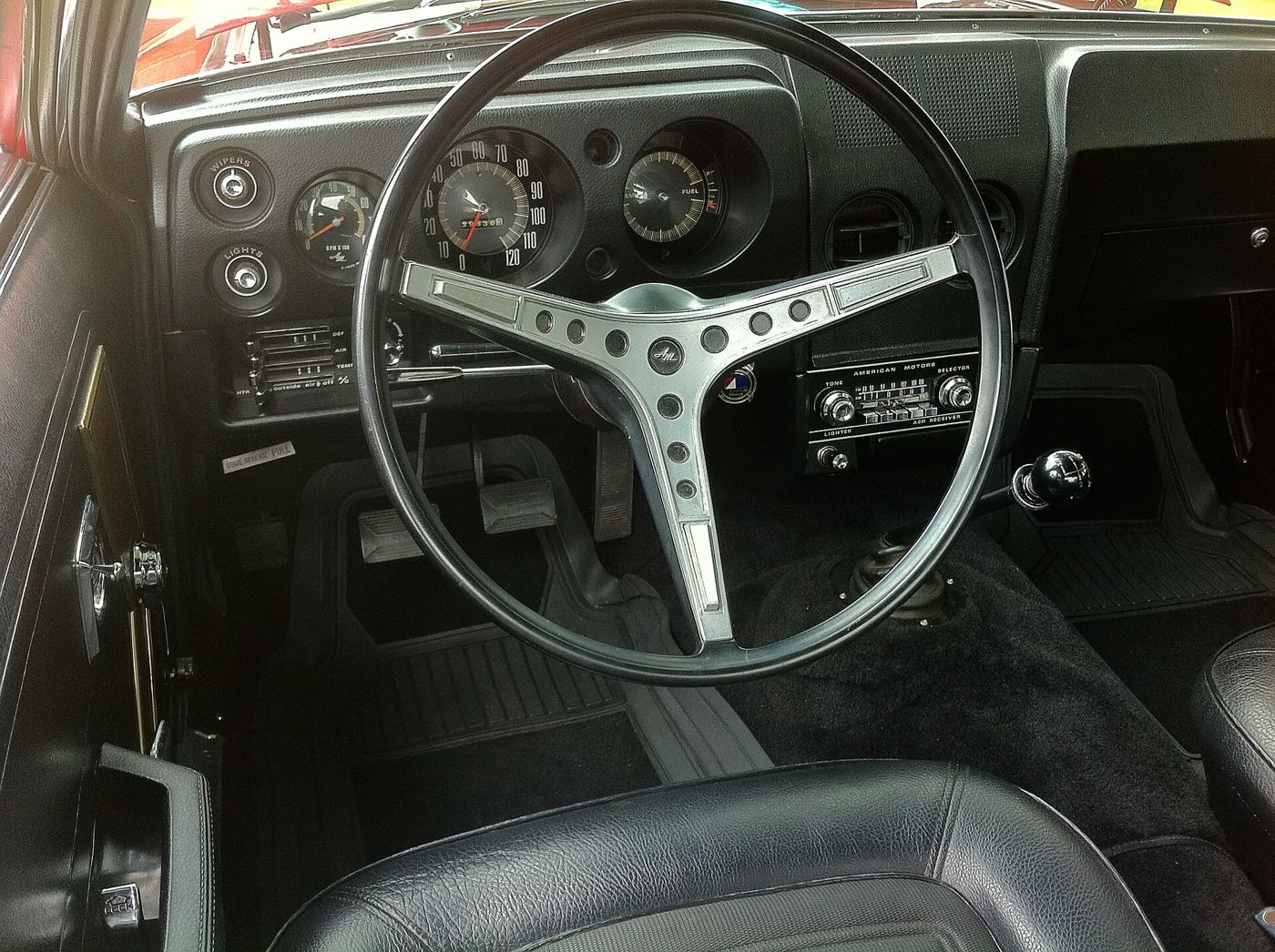 Black interior of a 1968 AMC AMX: three-spoke steering wheel, round gauges and black bucket seats
