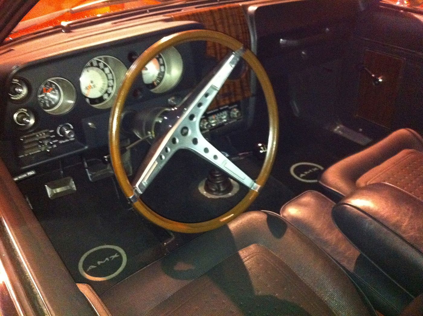 Dashboard of a 1969 AMC AMX with woodgrain-rim steering wheel, round gauges and tan bucket seats