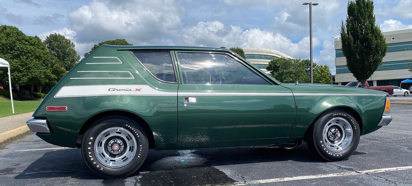 Green 1972 AMC Gremlin X in full side profile, with the white hockey-stick stripe carrying the Gremlin X script and slotted styled wheels