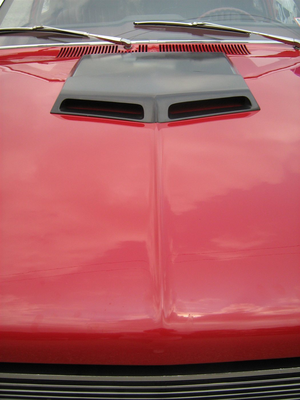 Close-up of the black ram-air hood scoop on a red 1971 AMC Hornet SC/360, with the windshield wipers and grille visible behind it