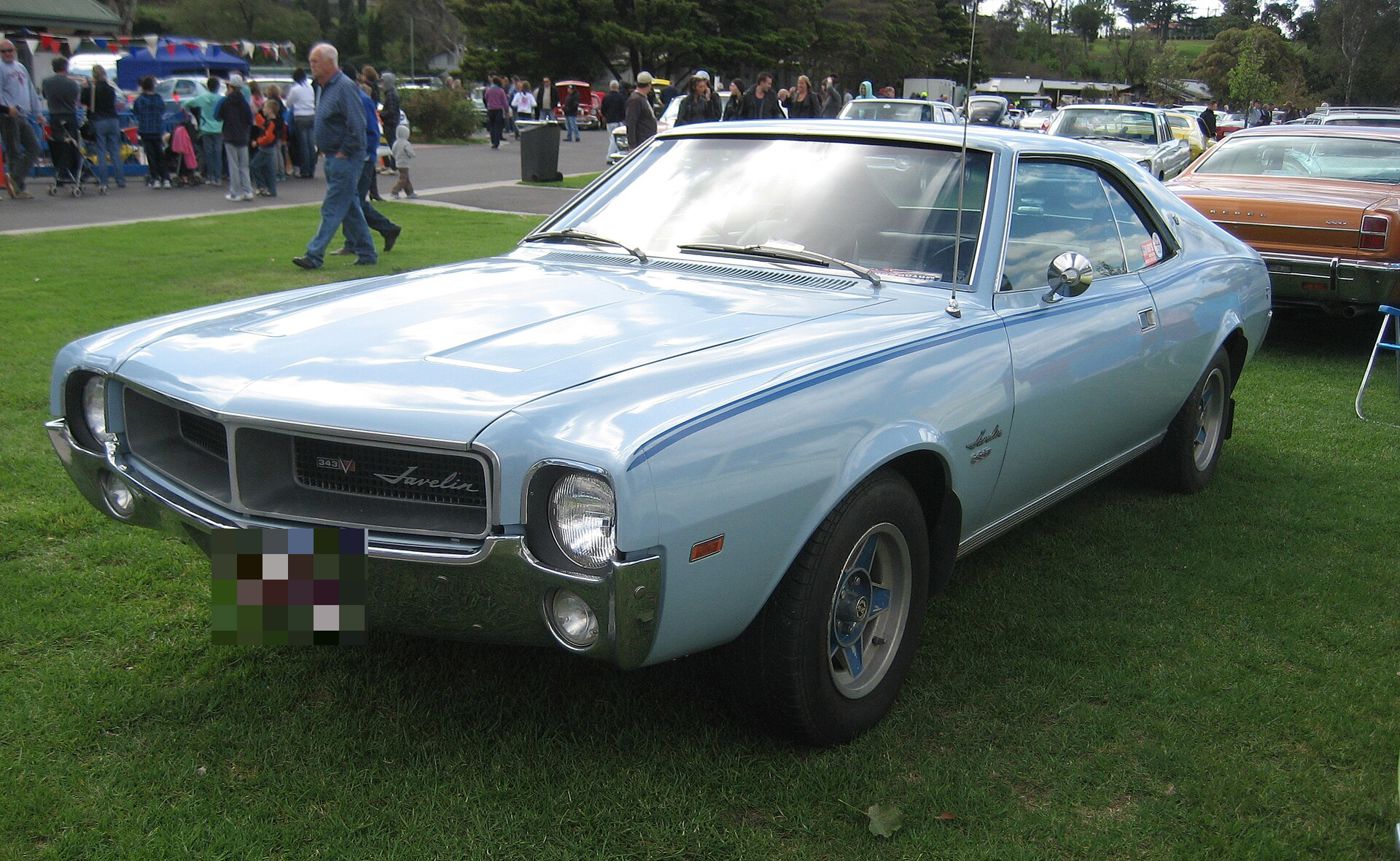 Light blue 1968 AMC Javelin hardtop from the front three-quarter on grass at a car show, with Javelin script and a 343 badge in the grille and a thin blue side stripe