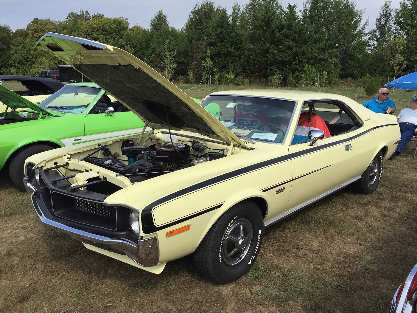 Pale-yellow 1970 AMC Javelin SST Mark Donohue edition with black side stripe and the hood open at an outdoor car show