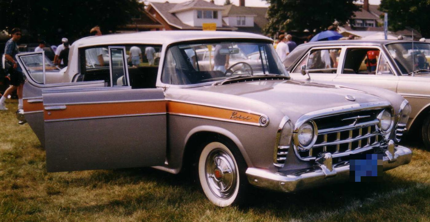 Silver 1957 Rambler Rebel four-door hardtop with gold anodized side trim and Rebel script, doors open at a car show