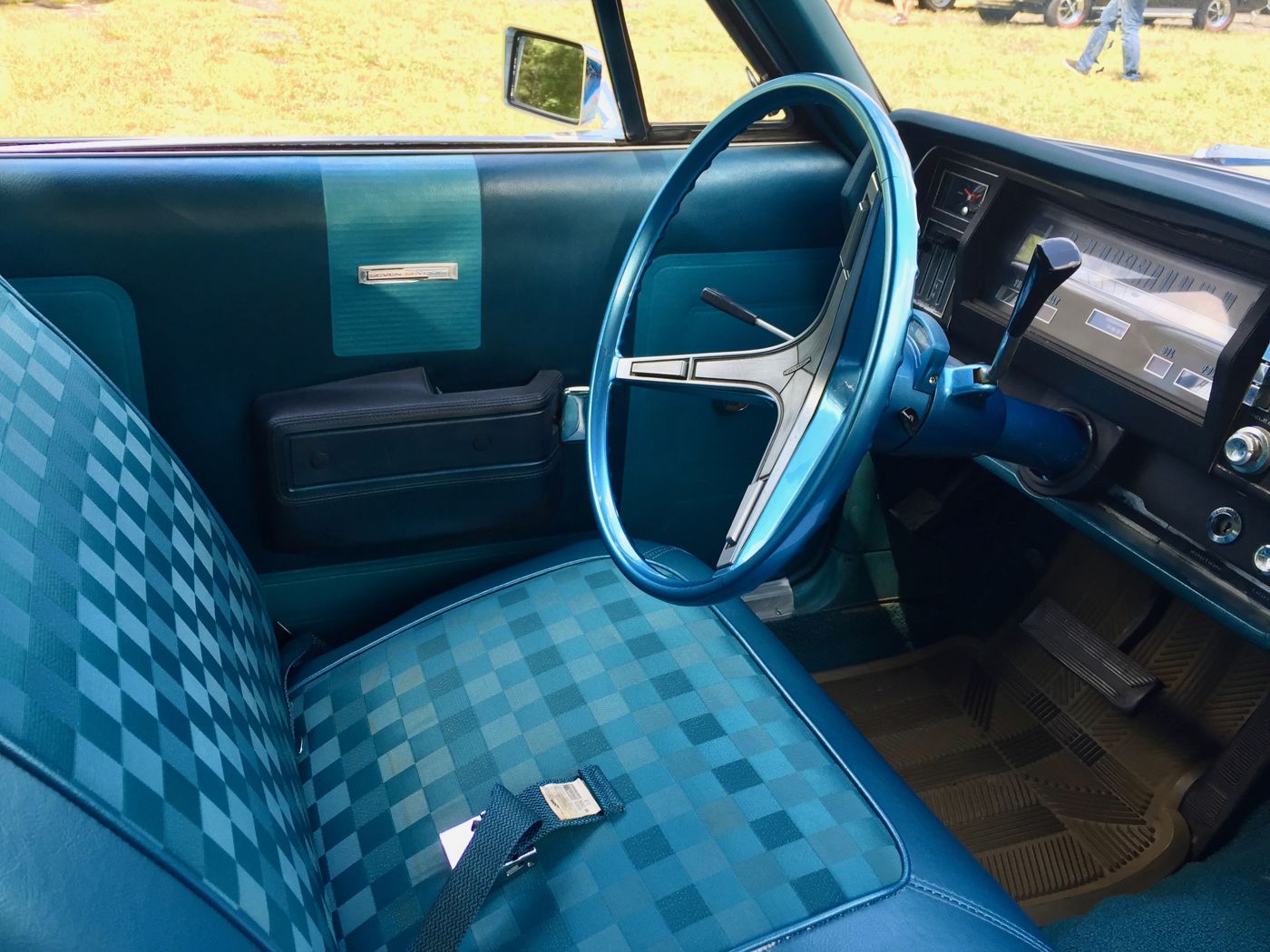 Interior of a blue 1968 AMC Rebel 770 showing the checked bench seat, door panel, steering wheel and dash