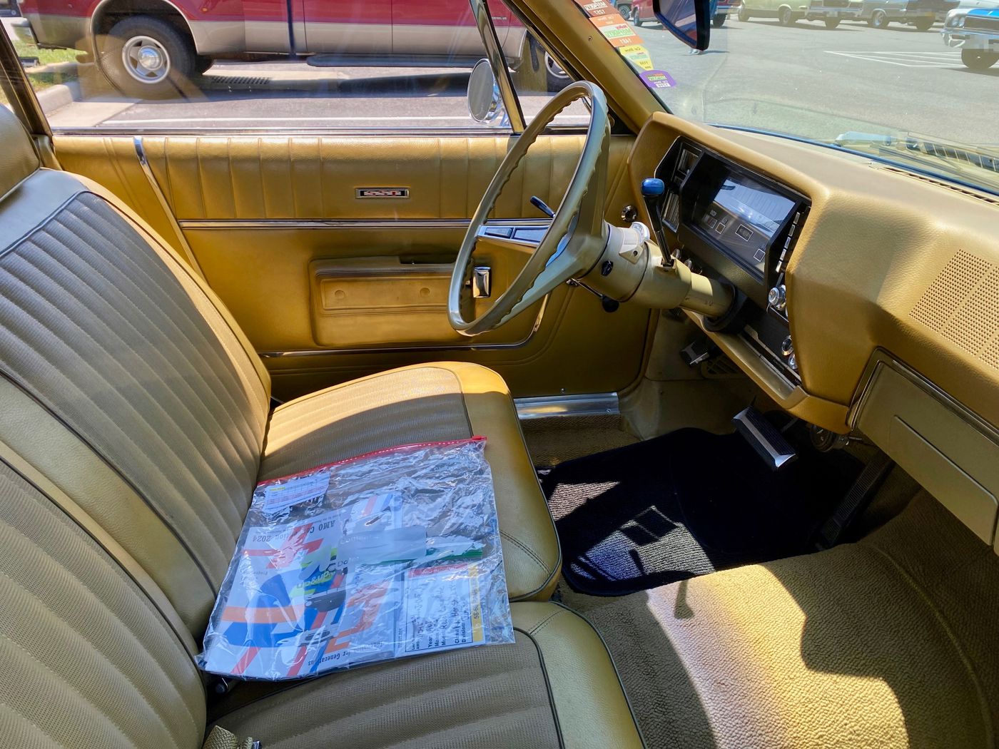 Interior of a gold 1968 AMC Rebel SST showing the vinyl bucket-style bench seat, SST door badge, steering wheel and dash