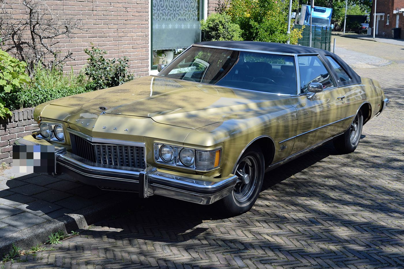 Gold 1974 Buick Riviera with dark vinyl top, front three-quarter, on a brick street