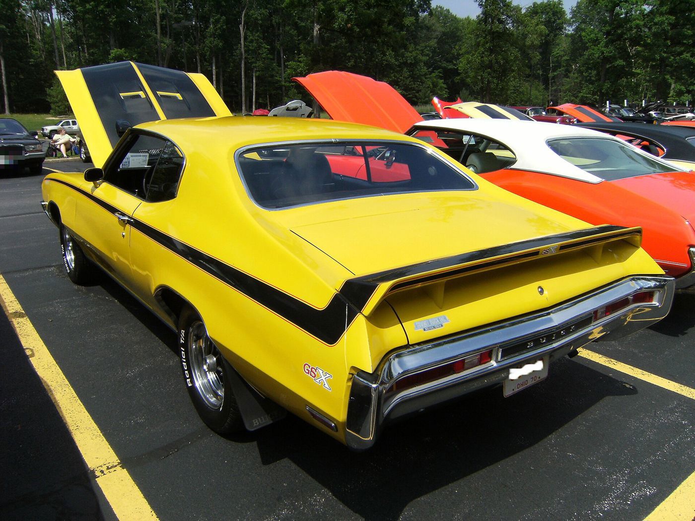 Saturn Yellow 1970 Buick GSX with black stripes and rear spoiler, rear three-quarter, hood open, at a car show