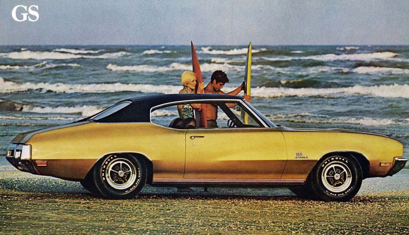 Brochure photo: gold 1971 Buick GS hardtop with Stage 1 fender badge on a beach, surfers behind