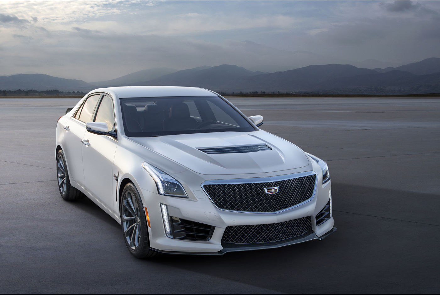 White 2016 Cadillac CTS-V sedan with carbon hood vent, front three-quarter, on an airfield with mountains behind