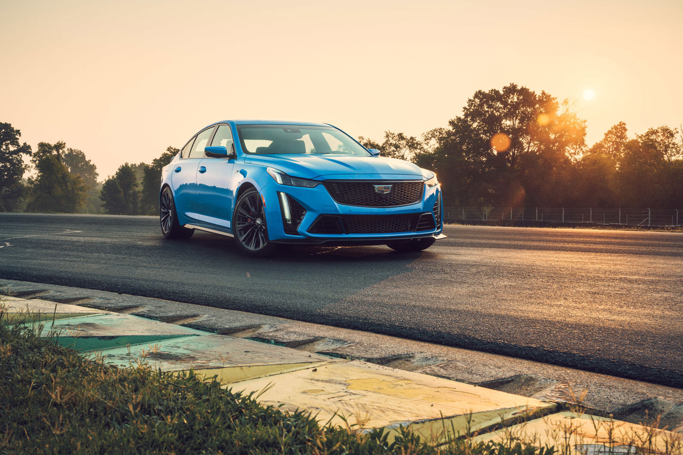 Electric-blue 2023 Cadillac CT5-V Blackwing sedan, front three-quarter, on a racetrack at sunset