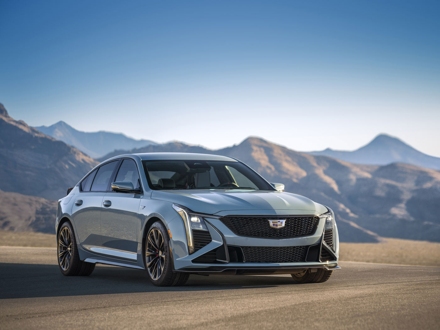 Light-blue-gray 2026 Cadillac CT5-V Blackwing with vertical lighting, front three-quarter, before mountains