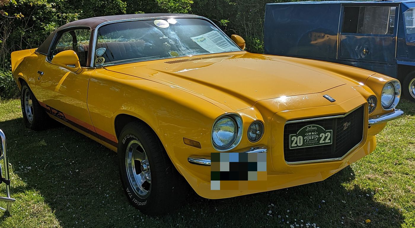 Yellow second-generation 1970 Chevrolet Camaro Z28 with a black vinyl roof, Z28 side stripe and grille badge, split front bumpers and rear spoiler, on grass at a British car show
