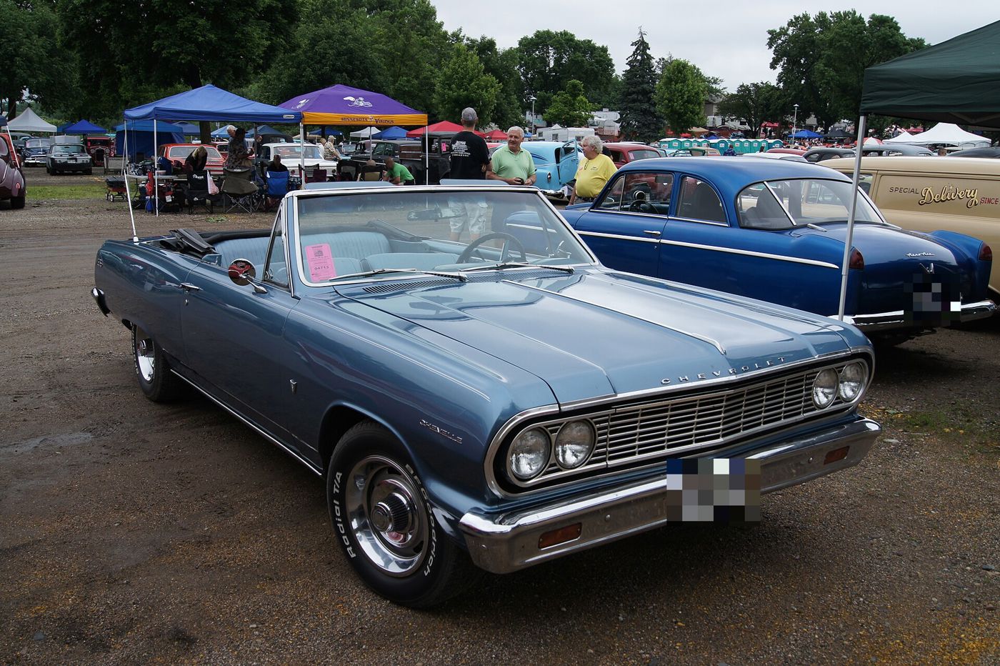 Light blue 1964 Chevrolet Chevelle Malibu convertible with the top down at an outdoor car show, front three-quarter, showing the 1964 grille and quad headlamps