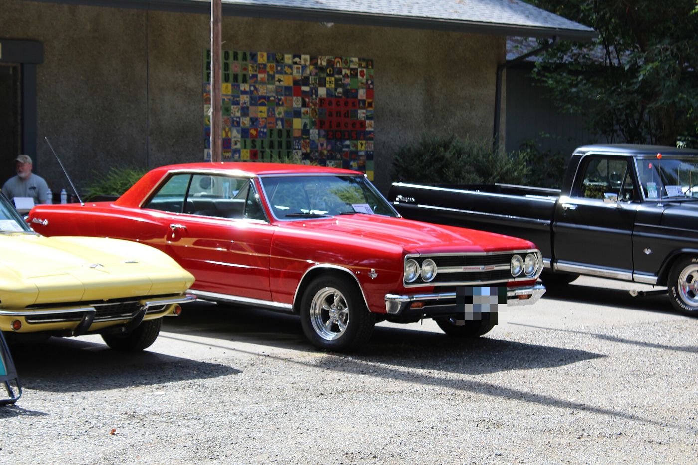 Red 1965 Chevrolet Chevelle Malibu SS two-door hardtop at a car show, front three-quarter, with the crossed-flags fender emblem and aftermarket five-spoke wheels