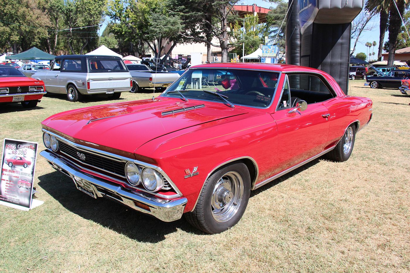 Red 1966 Chevrolet Chevelle SS 396 two-door hardtop on grass at a car show, front three-quarter, with the SS 396 grille badge, twin simulated hood scoops and 396 Turbo-Jet crossed-flags fender emblem
