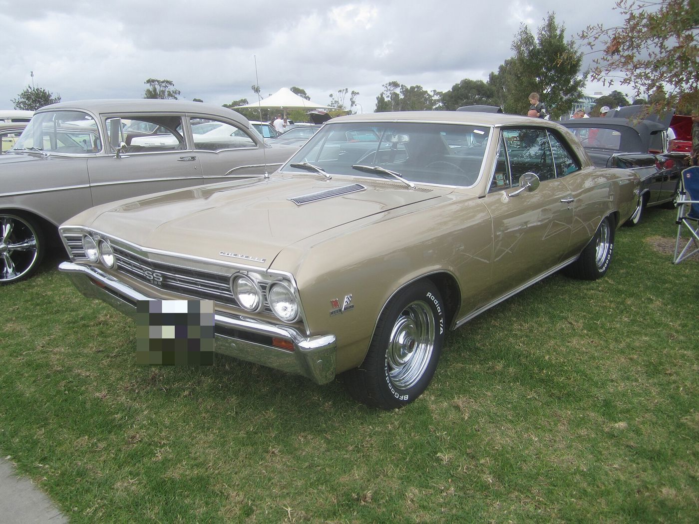 Gold 1967 Chevrolet Chevelle SS 396 two-door hardtop on grass at an Australian car show, front three-quarter, with the SS 396 grille badge, twin hood inserts and 396 Turbo-Jet fender emblem