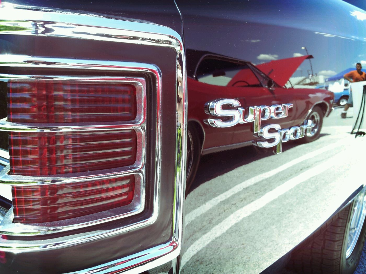 Close-up of the chrome Super Sport script on the black rear quarter panel of a 1967 Chevelle SS 396, beside the three-section taillamp, with a red Chevelle reflected in the paint