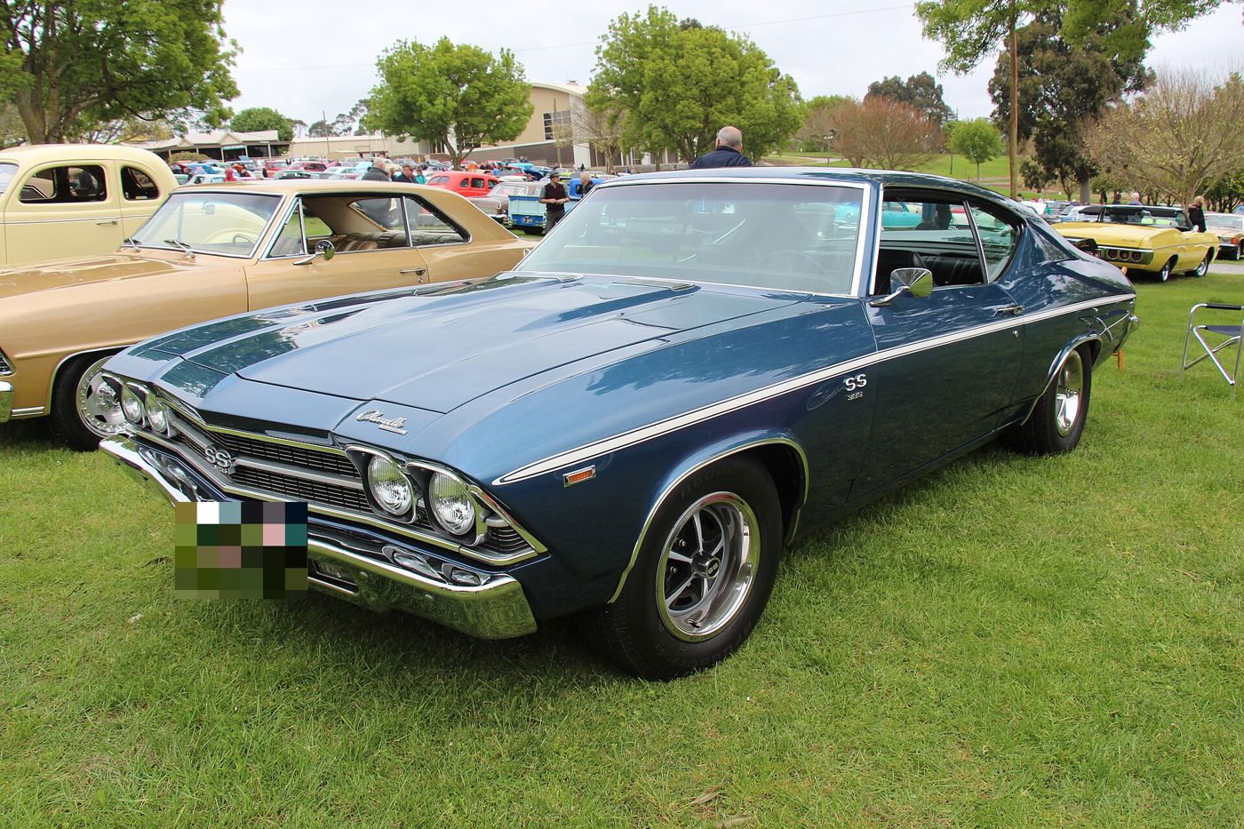 Dark blue 1969 Chevrolet Chevelle SS 396 two-door hardtop with a white side stripe on grass at a car show, front three-quarter, with SS 396 grille and fender badges and SS wheels