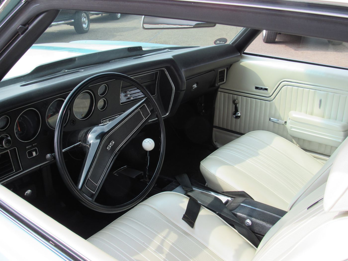 Interior of a 1970 Chevrolet Chevelle SS with white bucket seats, SS steering wheel, SS door-panel badge, four-speed floor shifter with white knob, and round gauges in a black dash