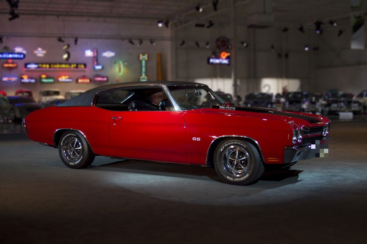 Red 1970 Chevrolet Chevelle SS two-door hardtop with a black vinyl roof, black hood stripes, SS fender badge and Magnum 500-style wheels, displayed in the GM Heritage Center hall