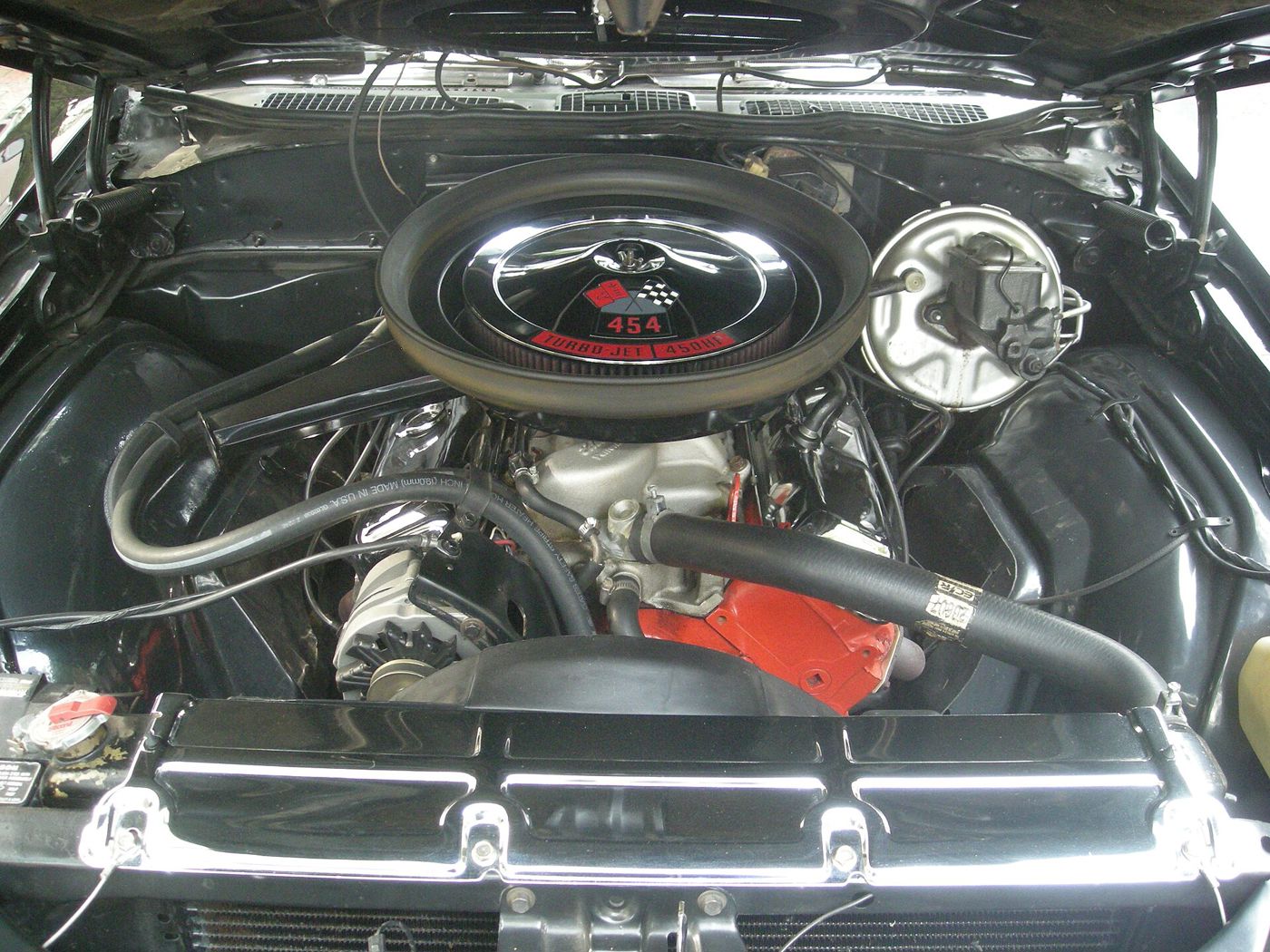 Engine bay of a black 1970 Chevrolet Chevelle SS 454 with an orange 454 big-block under a black air cleaner whose decal reads 454 Turbo-Jet 450 HP, the LS6 rating
