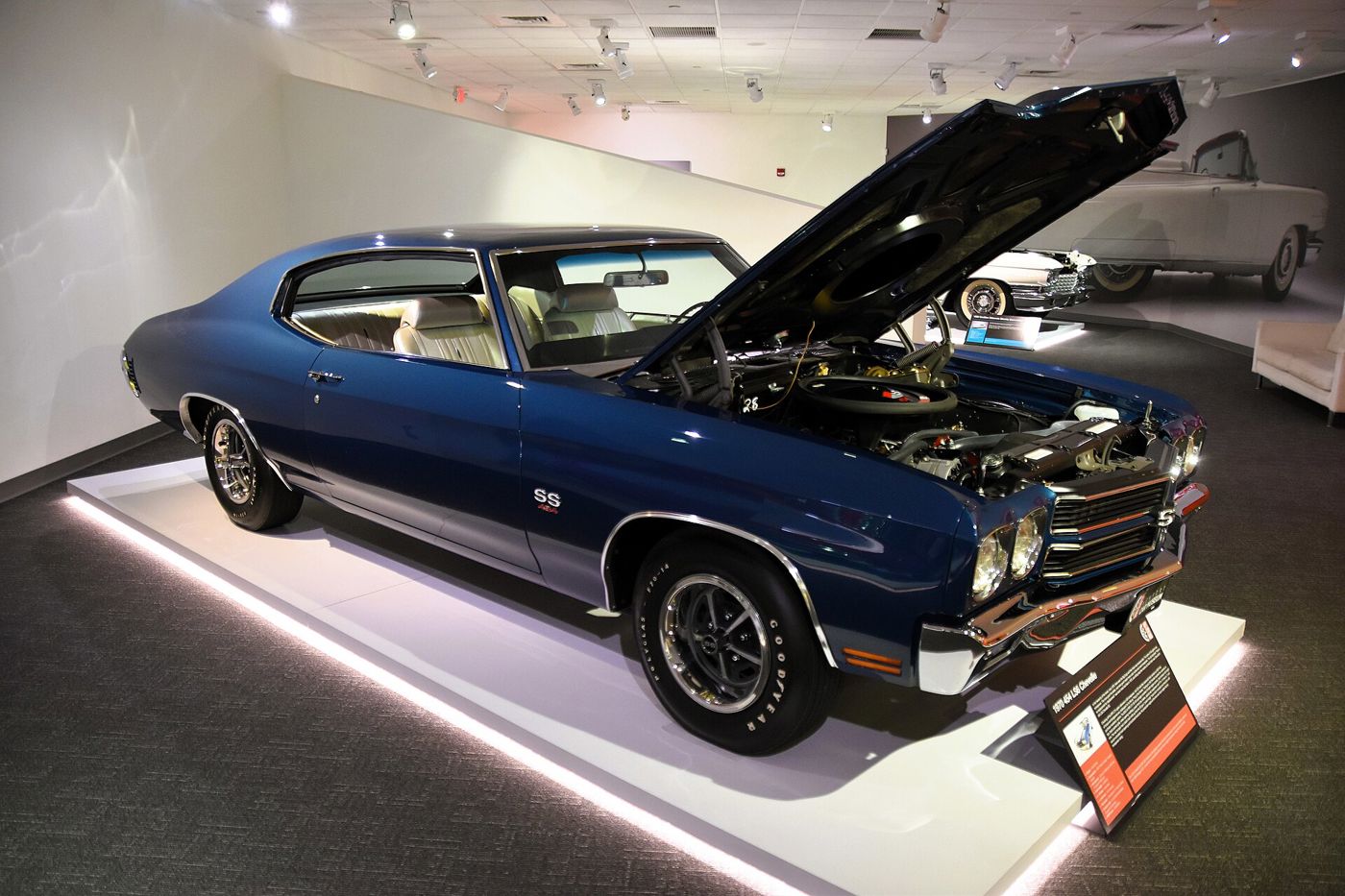 Dark blue 1970 Chevrolet Chevelle SS 454 on a lit museum plinth with its hood raised over the LS6 engine, SS 454 fender badge, SS wheels and a display placard titled 1970 454 LS6 Chevelle