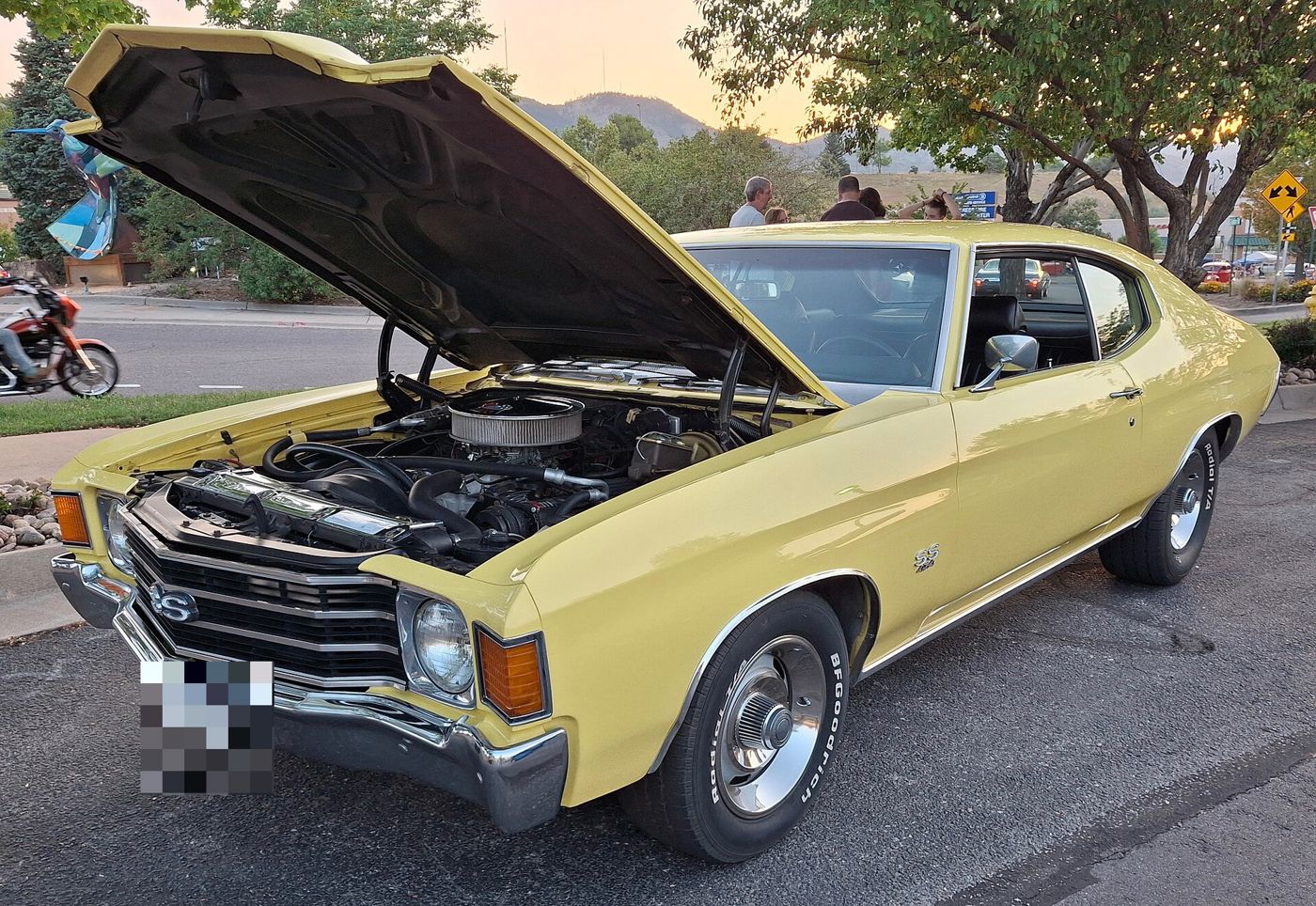 Yellow 1972 Chevrolet Chevelle SS 454 two-door hardtop at an evening car show, front three-quarter with the hood raised over the big-block V8, showing the SS grille badge, SS 454 fender badge and Rally wheels