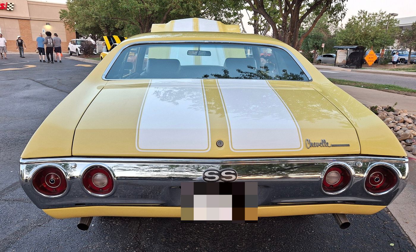 Rear of a yellow 1972 Chevrolet Chevelle SS 454 with white trunk stripes, showing the SS emblem in the chrome bumper, the four round taillamps, the Chevelle script on the trunk lid and a cowl-induction hood seen over the roof