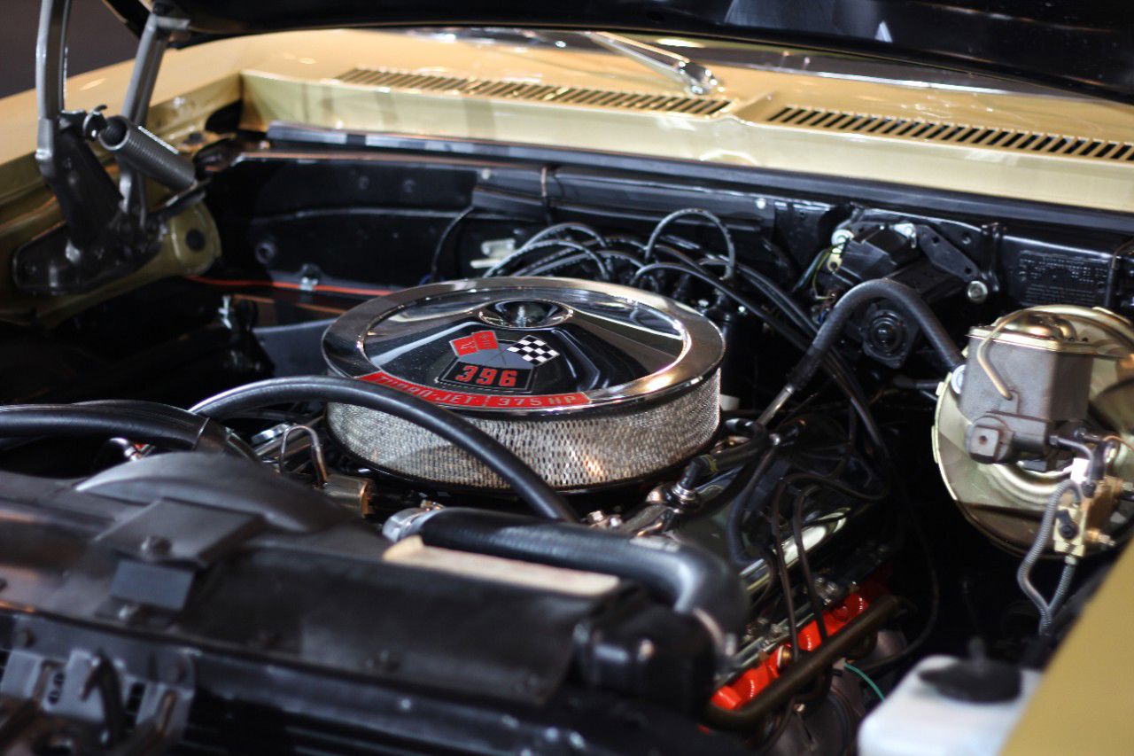 Engine bay of a gold 1970 Chevrolet Nova SS with the 396 V8 under a chrome open-element air cleaner whose decal reads 396 Turbo-Jet 375 HP