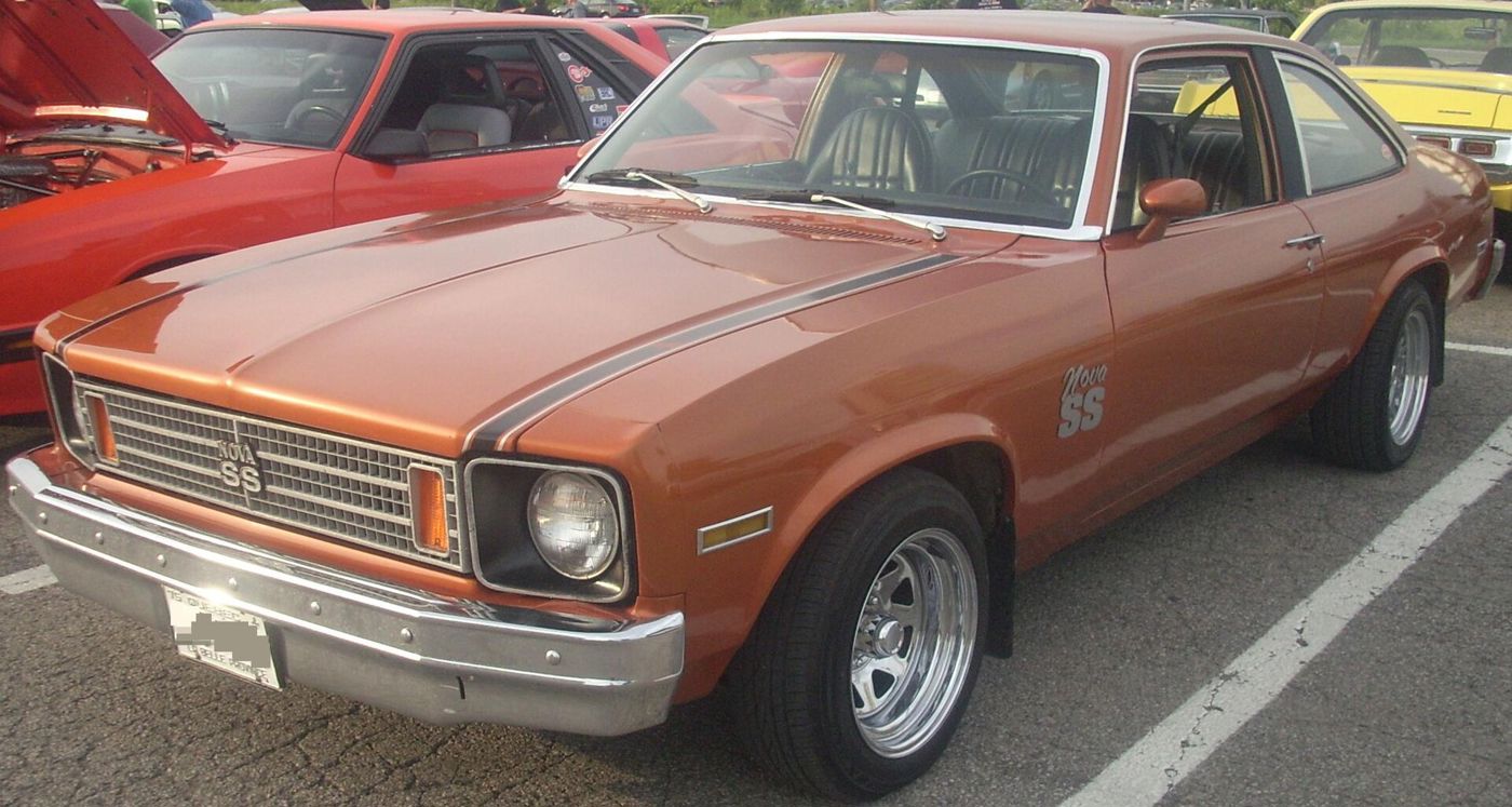 Copper 1975 Chevrolet Nova SS coupe in a car-show parking lot, front three-quarter, with the egg-crate grille, Nova SS grille badge and Nova SS fender decal