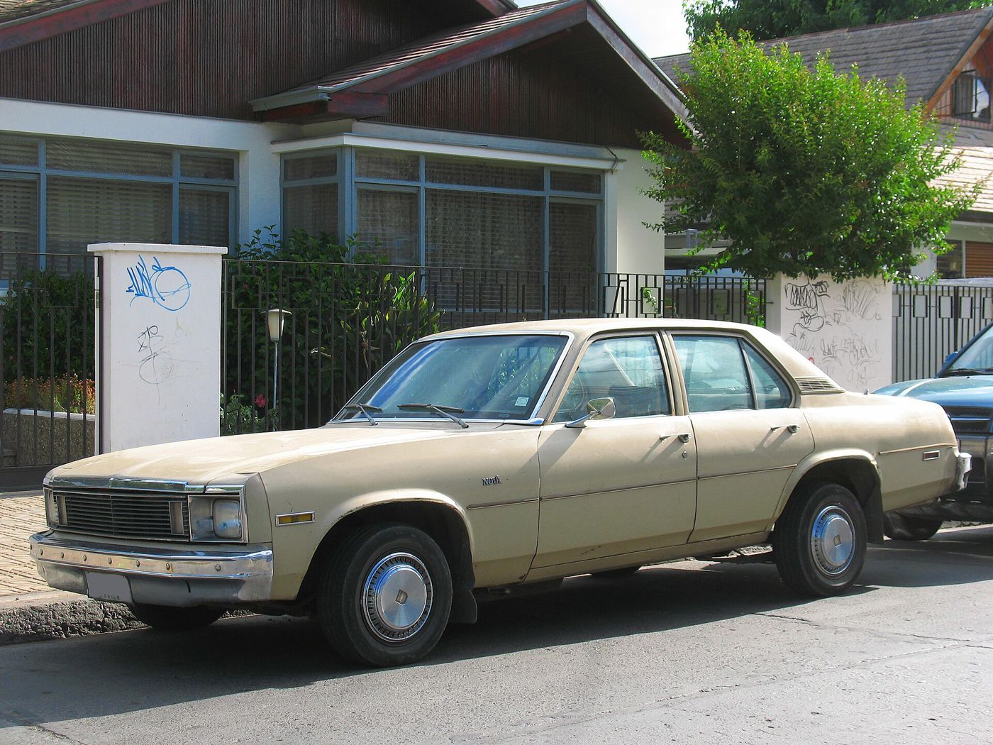 Beige 1979 Chevrolet Nova four-door sedan parked at a curb in Chile, front three-quarter, showing the final-year rectangular headlamps and grille