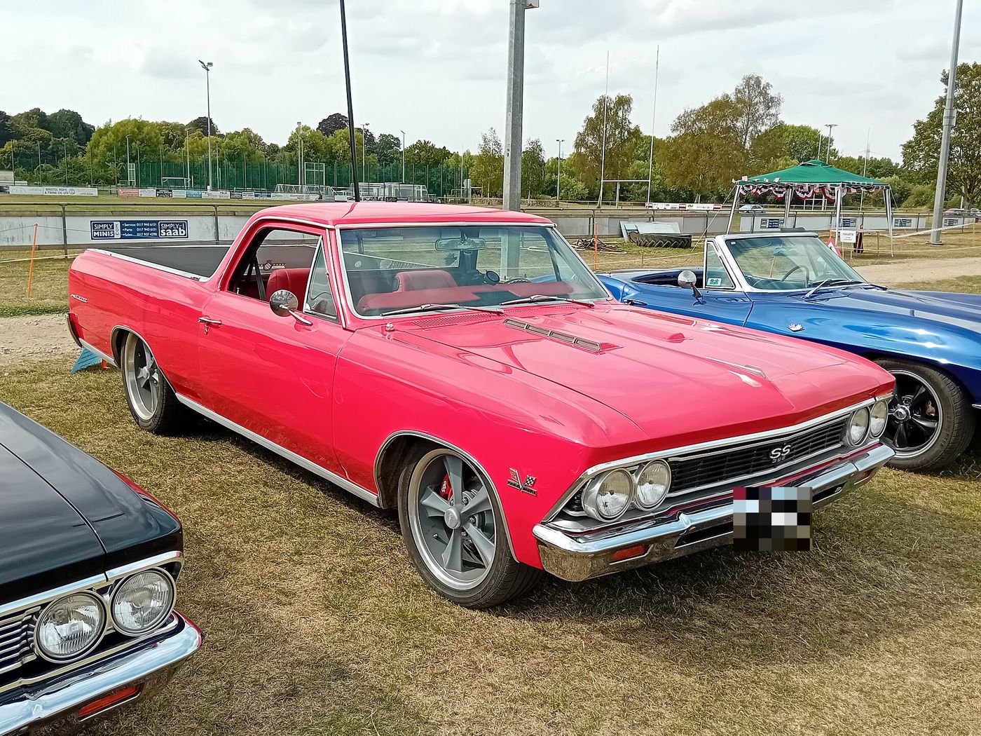 Red 1966 Chevrolet El Camino on grass at a British car show, front three-quarter, with the SS 396 grille badge, crossed-flags fender emblem and aftermarket wheels with red brake calipers