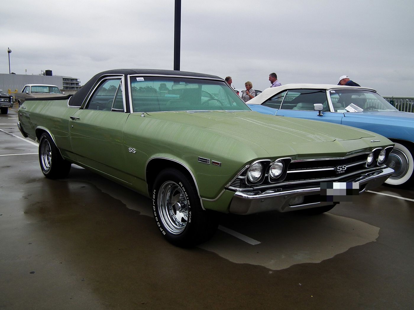 Green 1969 Chevrolet El Camino SS 396 with a black vinyl roof on a wet parking deck, front three-quarter, with the SS 396 grille badge and SS fender emblem