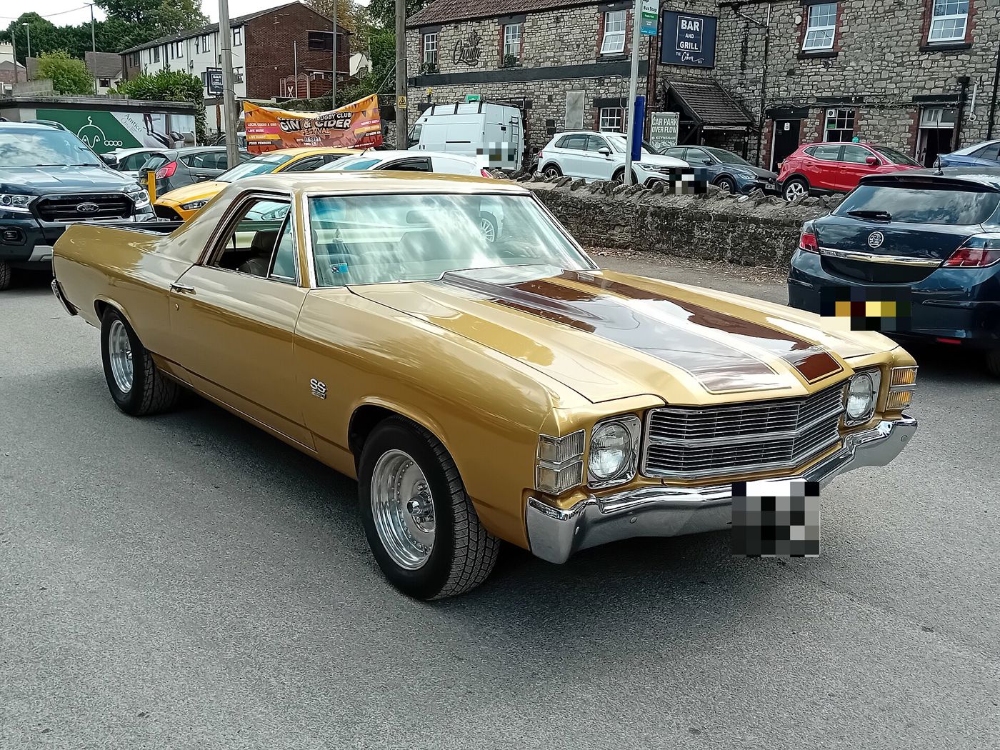 Gold 1971 Chevrolet El Camino SS with brown hood stripes in an English pub car park, front three-quarter, showing the single-headlamp 1971 front end and SS fender badge