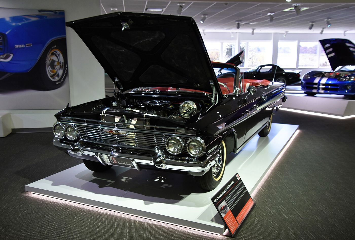 Black 1961 Chevrolet Impala SS 409 convertible with red interior on a museum plinth, hood raised over the 409 V8, with the museum placard naming it