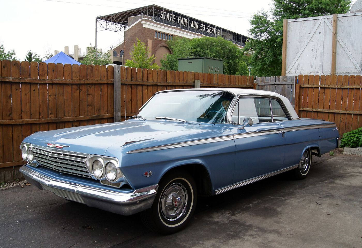 Light blue 1962 Chevrolet Impala two-door hardtop with a white roof, front three-quarter view, showing the crossed-flags V8 emblem on the front fender