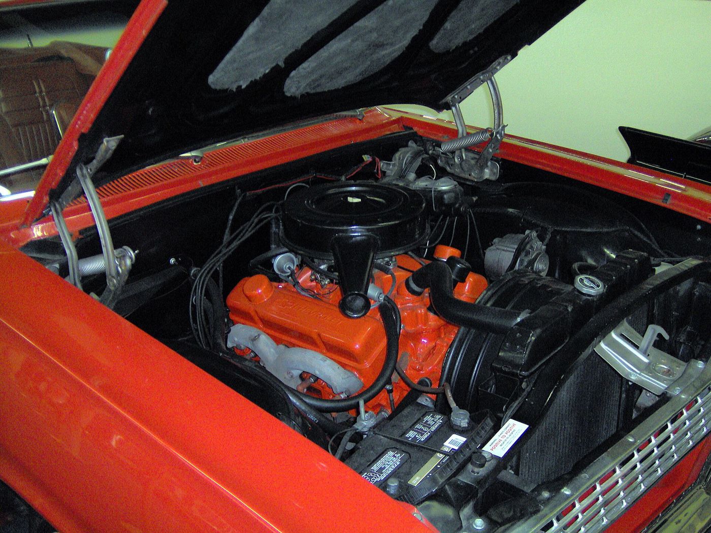 Orange Chevrolet small-block V8 under a black air cleaner in the engine bay of a red 1963 Chevrolet Impala Super Sport convertible, hood raised
