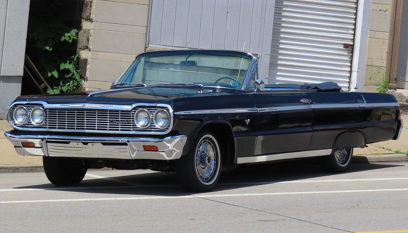 Black 1964 Chevrolet Impala SS convertible with the top down, parked at a curb, front three-quarter, showing the 1964 grille and full wheel covers