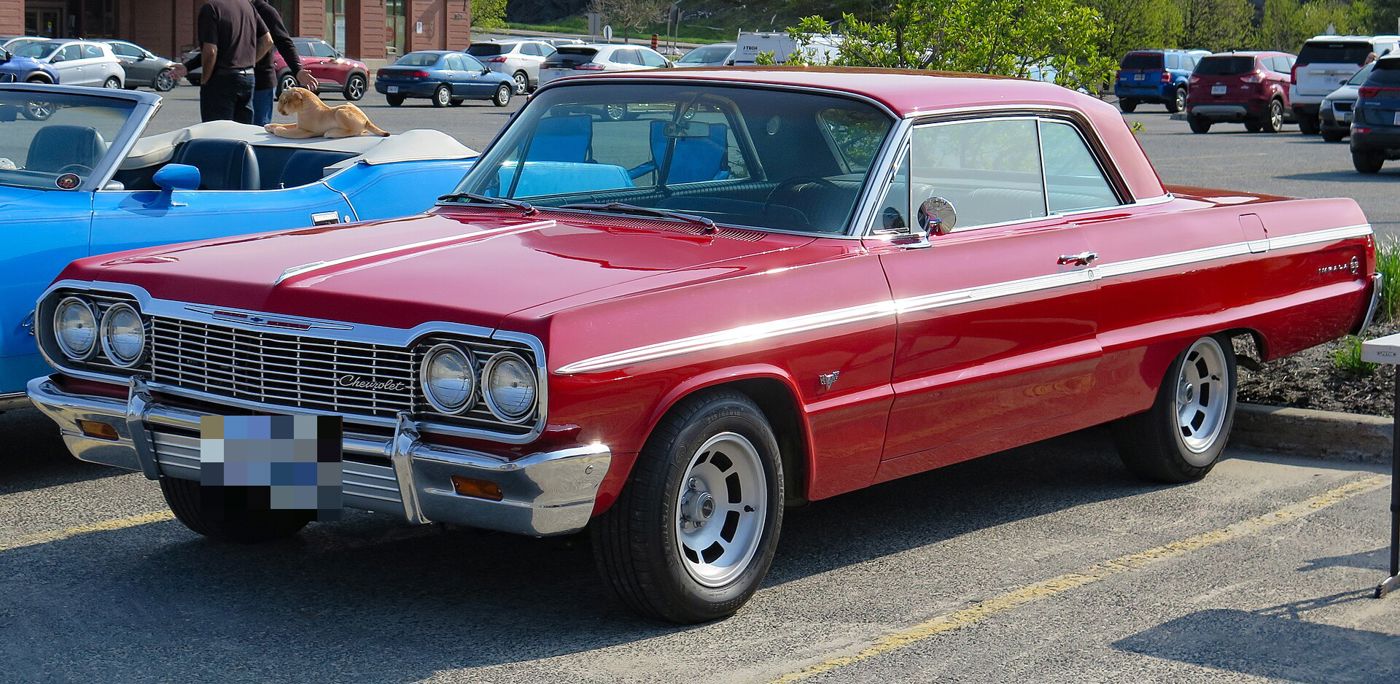 Red 1964 Chevrolet Impala SS two-door hardtop at a car show, front three-quarter, with Impala SS emblem on the rear quarter and aftermarket slotted alloy wheels
