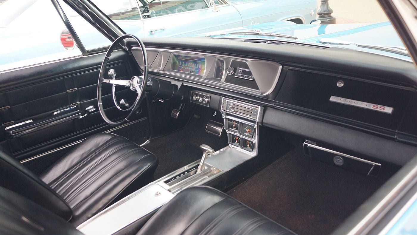 Black interior of a 1966 Chevrolet Impala SS showing bucket seats, the center console with floor shifter and four auxiliary gauges, and the Impala SS nameplate on the dashboard