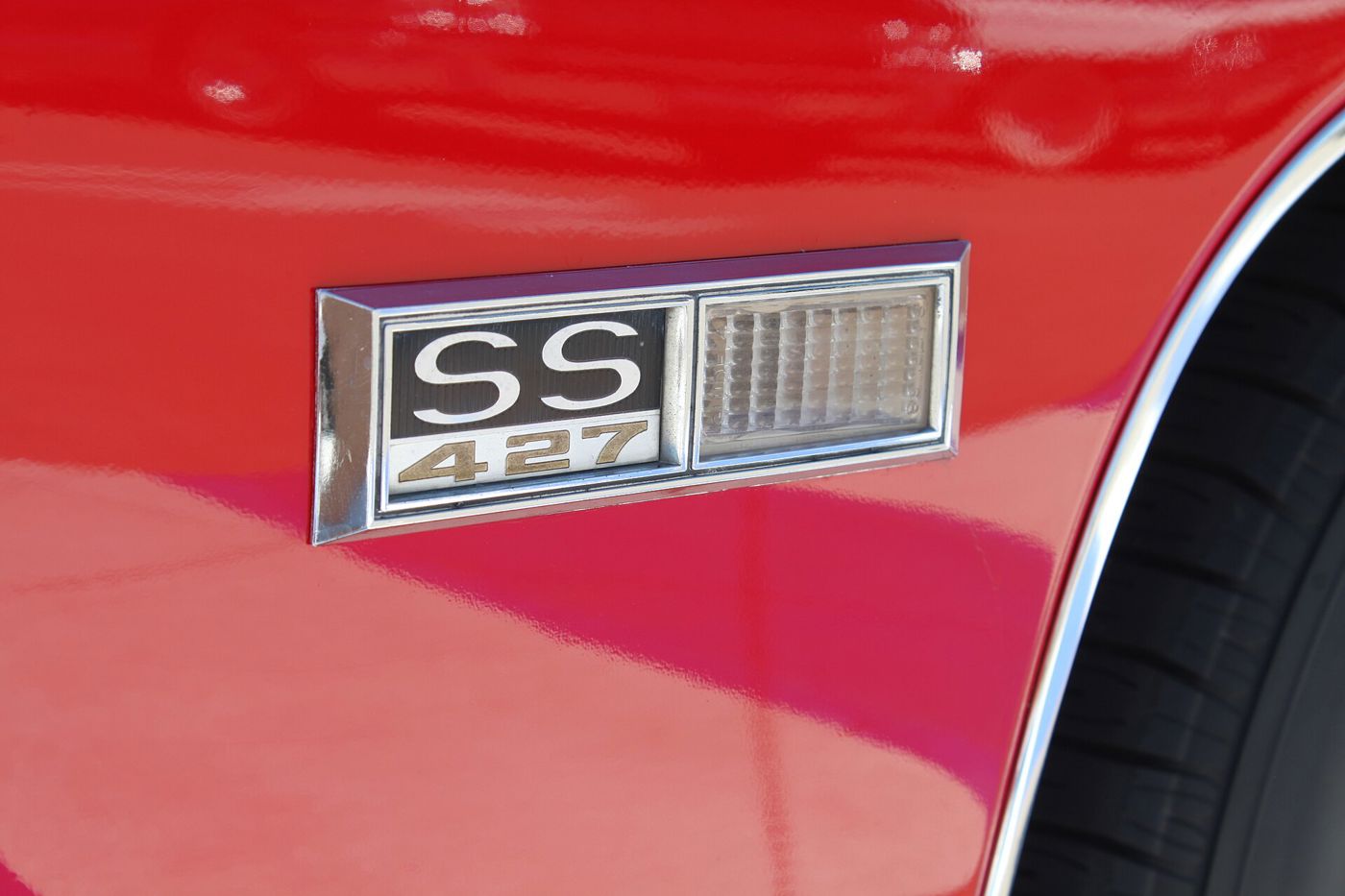 Close-up of the chrome SS 427 badge with integrated side marker lamp on the red front fender of a 1968 Chevrolet Impala SS 427