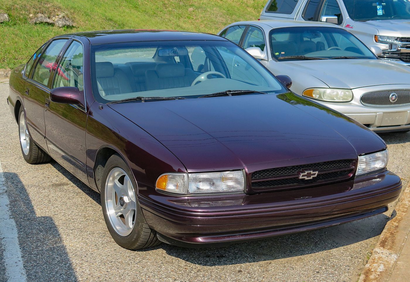 Dark Cherry Metallic 1996 Chevrolet Impala SS four-door sedan parked at a curb, front three-quarter, showing the body-color grille with bowtie and the five-spoke 17-inch alloy wheels