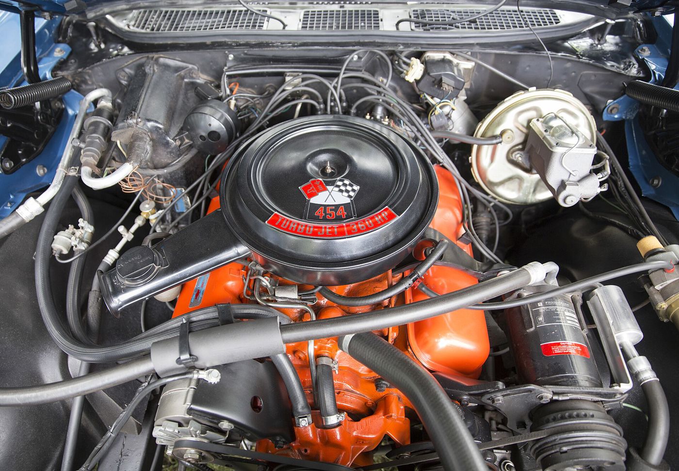 Orange 454 V8 in the engine bay of a blue 1970 Chevrolet Monte Carlo SS, with its black air cleaner decal reading 454 Turbo-Jet 360 HP and the crossed-flags emblem