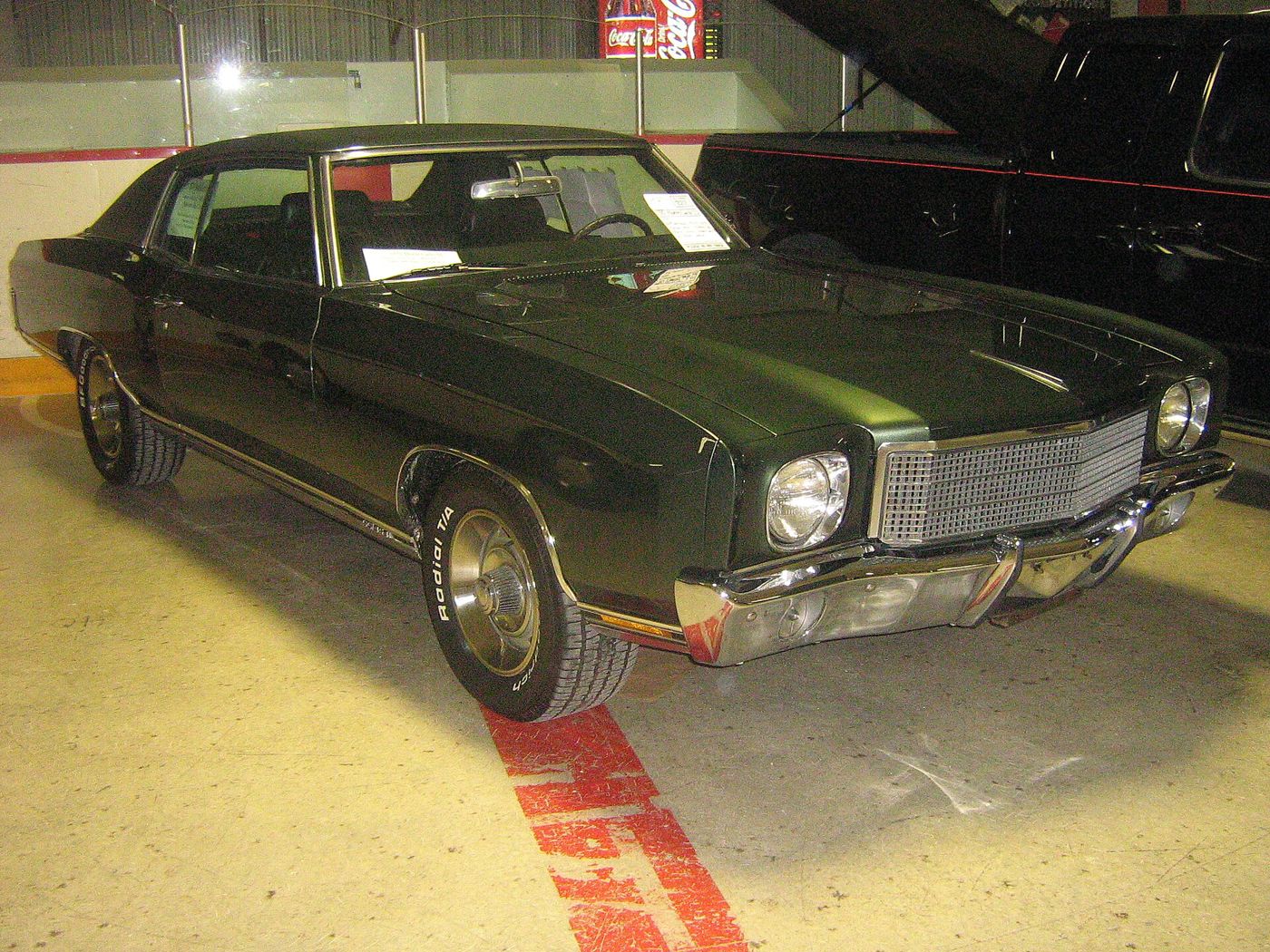 Dark green 1970 Chevrolet Monte Carlo two-door hardtop with black vinyl roof at an indoor show, front three-quarter, with the SS 454 badge on the rocker trim and Rally wheels