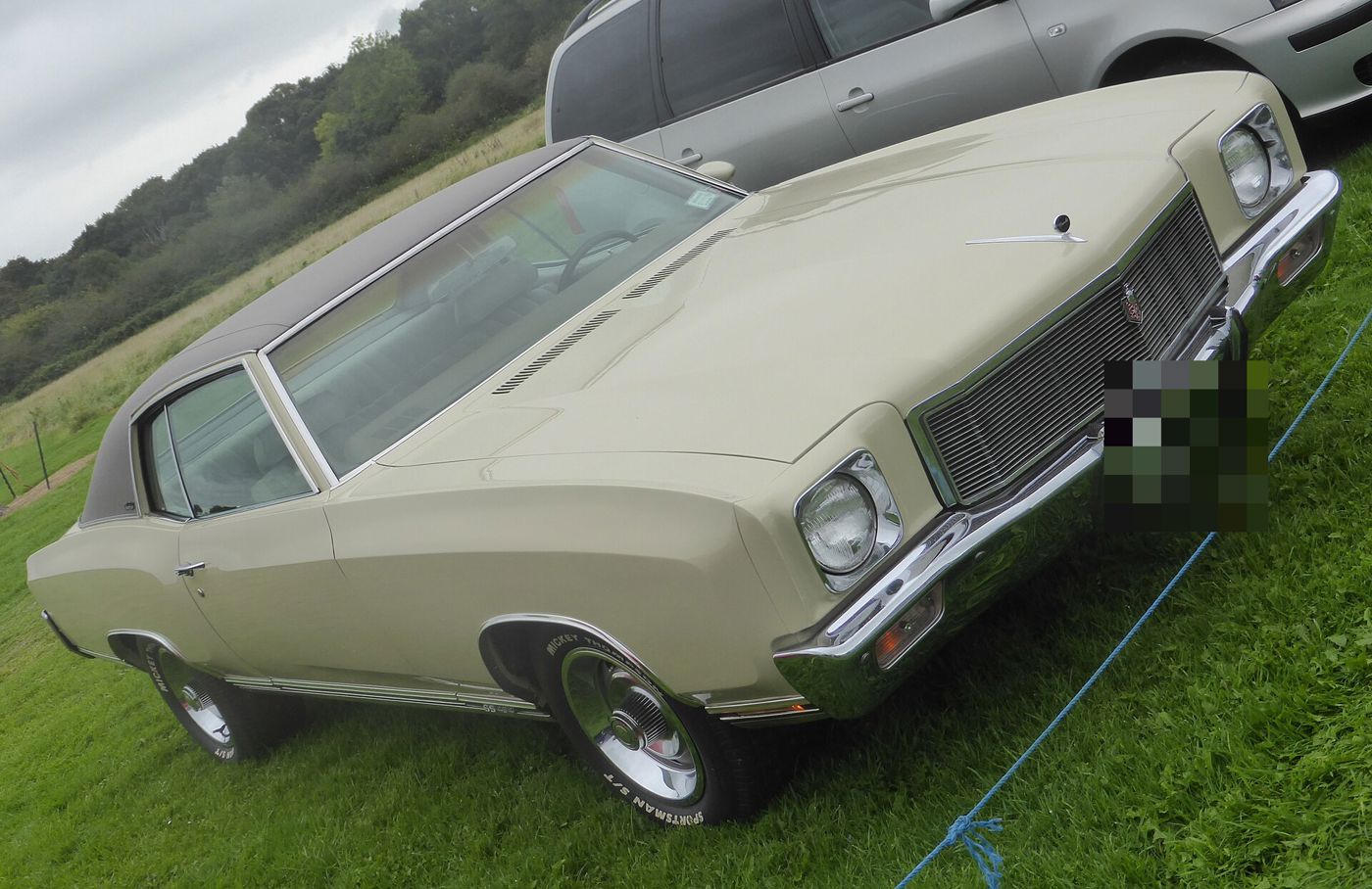 Cream 1971 Chevrolet Monte Carlo SS two-door hardtop with a dark vinyl roof, parked on grass at a show, front three-quarter, with the SS 454 rocker badge and Rally wheels