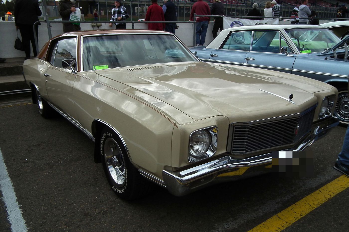 Cream 1971 Chevrolet Monte Carlo two-door hardtop with a brown vinyl roof at a car show, front three-quarter, showing the 1971 fine-bar grille and single round headlamps