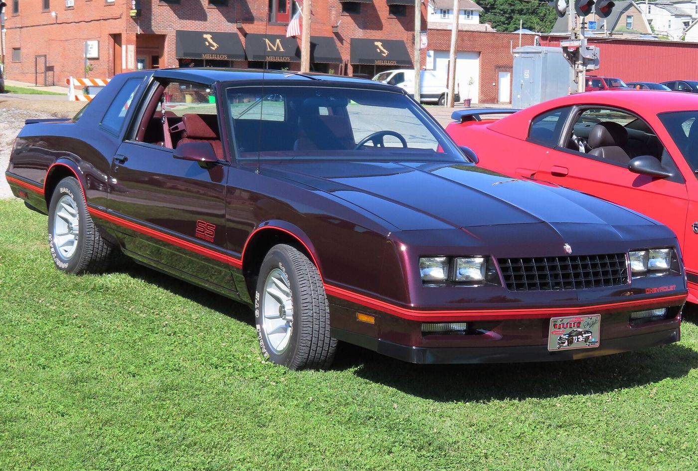 Dark maroon 1987 Chevrolet Monte Carlo SS Aerocoupe on grass at a car show, front three-quarter, showing the steeply raked rear window, SS door lettering and red pinstripes