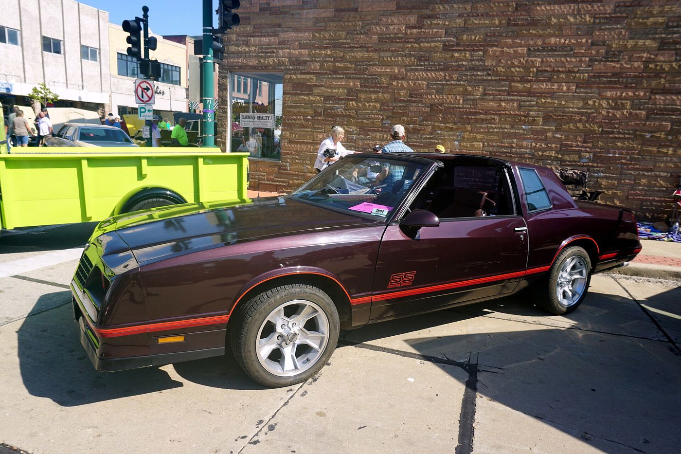 Dark maroon 1987 Chevrolet Monte Carlo SS with red pinstripes and SS Monte Carlo door lettering at a downtown car show, side view, with the aero nose and aftermarket five-spoke wheels