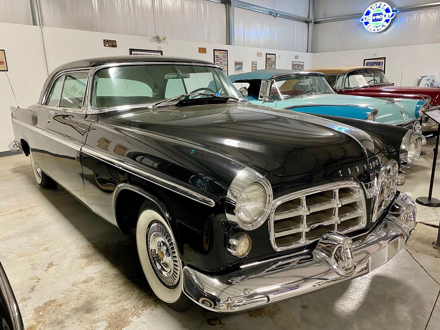 Black 1955 Chrysler C-300 hardtop with its large egg-crate grille and wide whitewall tyres, in a museum hall